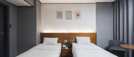 A hotel room with two single beds, a wooden headboard, a small table, and a chair.