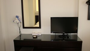 Habitación de hotel con cómoda de madera oscura, televisión de pantalla plana, espejo y secador de pelo en la pared.