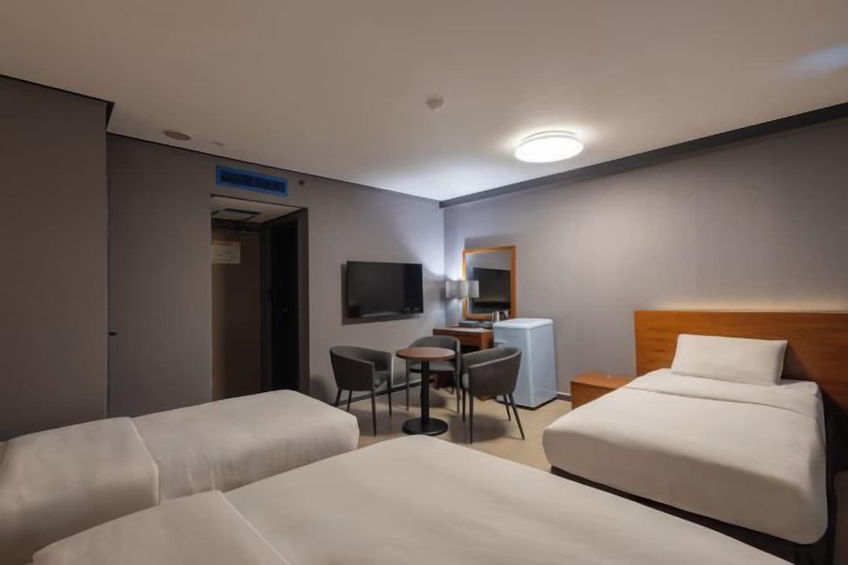A hotel room with two beds, a desk, a chair, a TV, and a mirror.