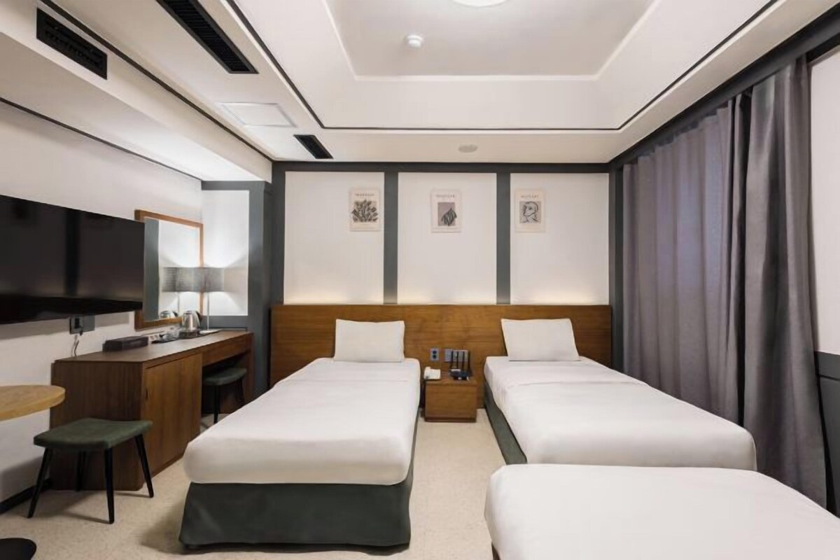 A hotel room with two beds, a desk, a TV, and artwork on the walls.