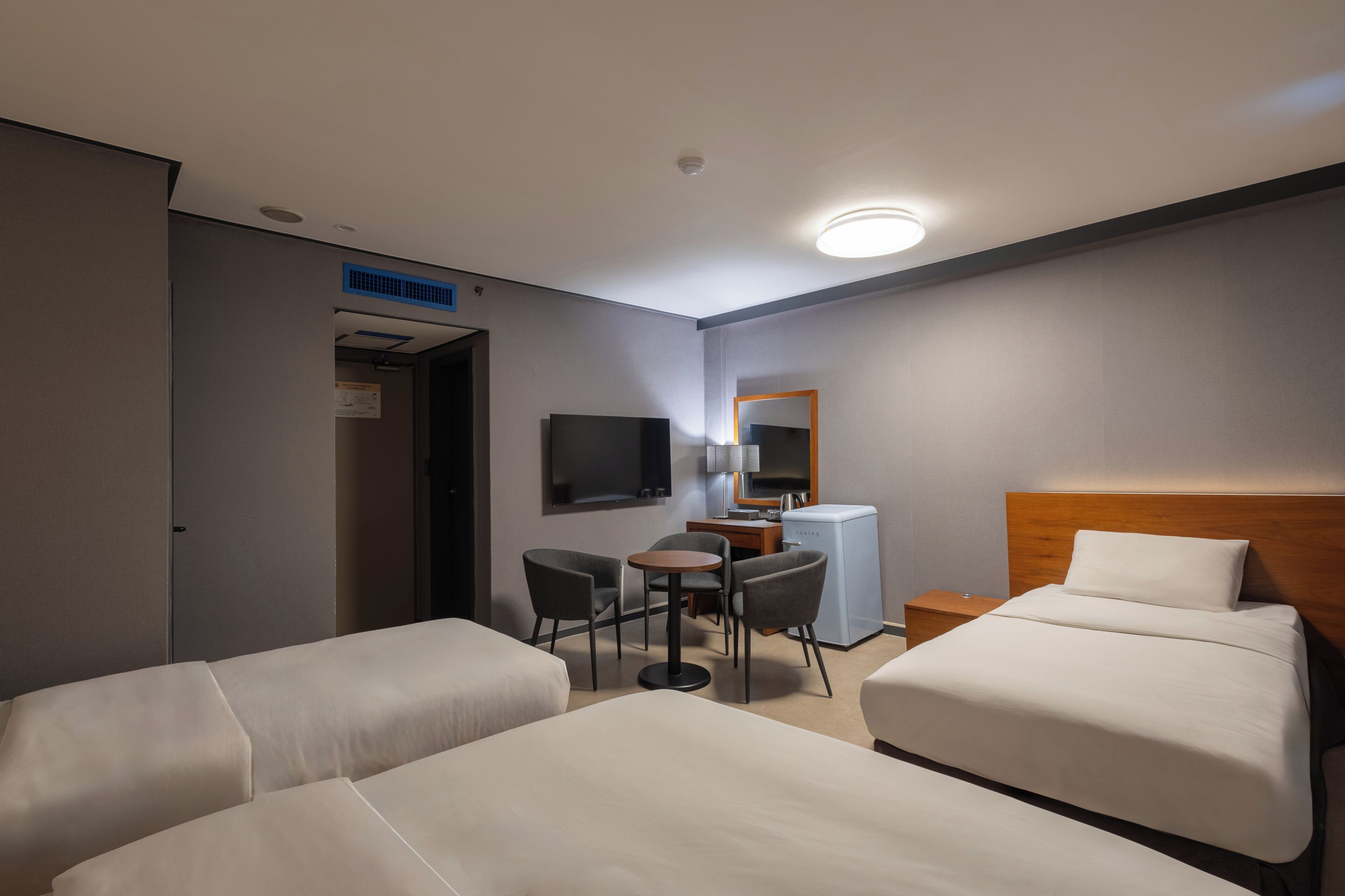 Habitación de hotel con dos camas, un escritorio con silla, televisor y refrigerador pequeño.