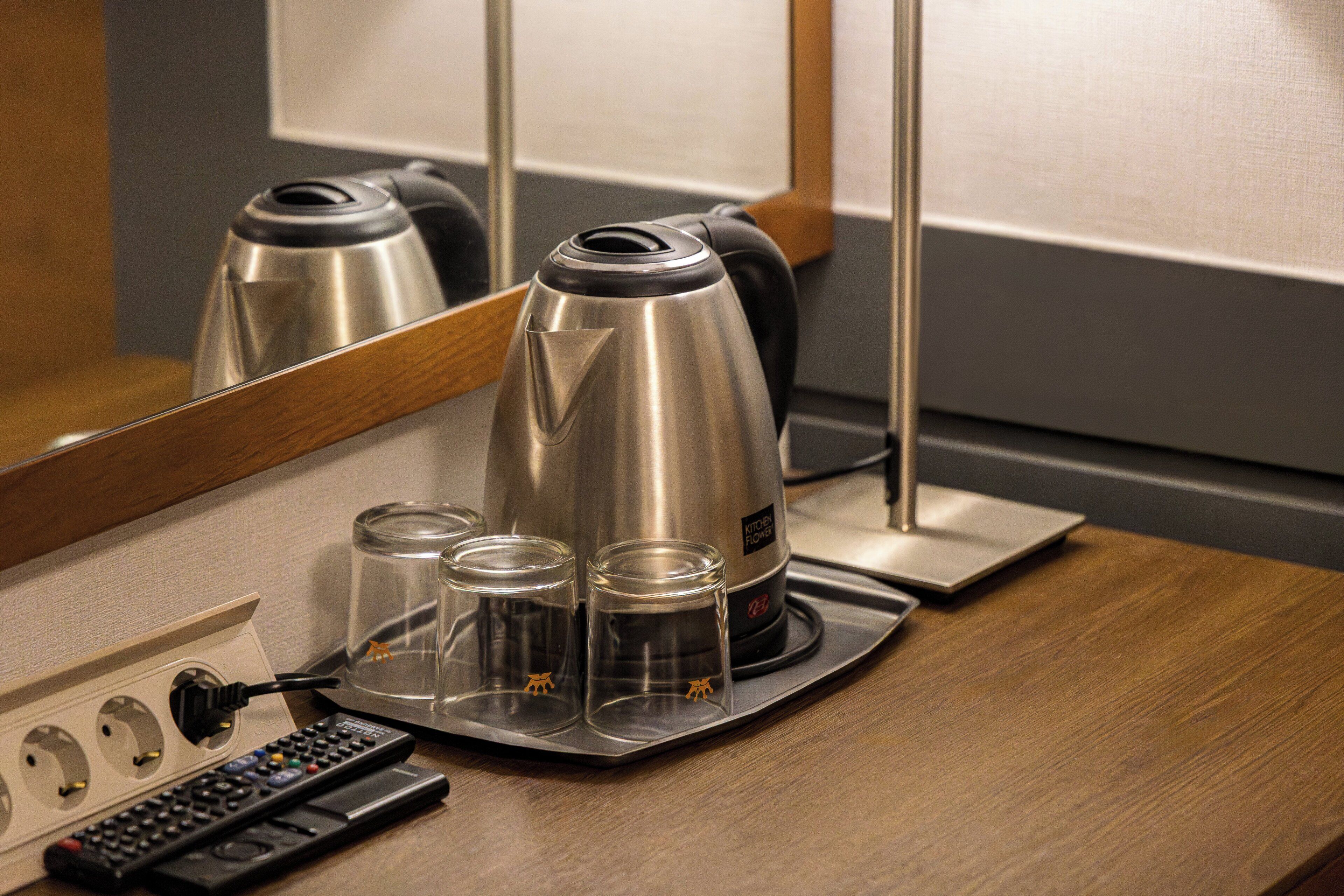 A hotel room with a coffee maker, a remote control, and a tray with glasses and a bottle.