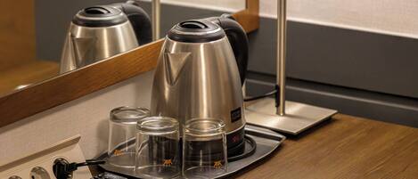 A hotel room with a coffee maker, a remote control, and a tray with glasses and a bottle.