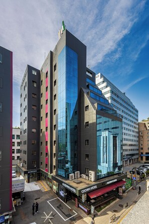 Un hotel moderno con fachada de vidrio, varios pisos y una terraza en la azotea.