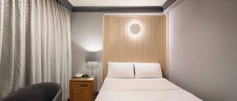 A hotel room with a bed, a chair, a nightstand, a lamp, and a window with curtains.