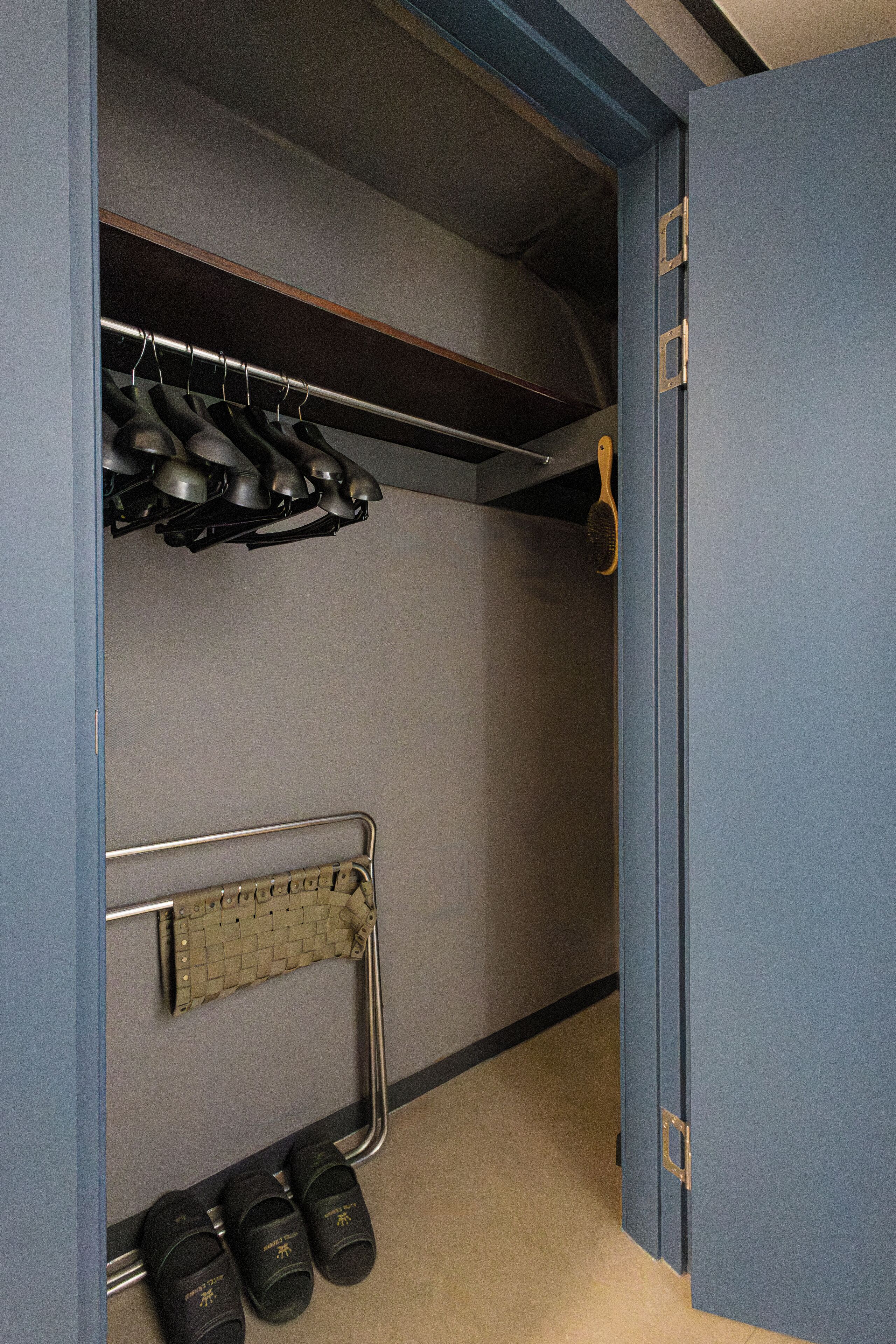 Un placard de rangement avec des étagères pour suspendre des vêtements, un porte-chaussures en métal et une paire de chaussures posées sur le sol.