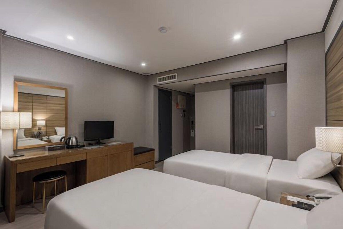 A hotel room with two beds, a desk with a computer, a mirror, and a door leading to a bathroom.
