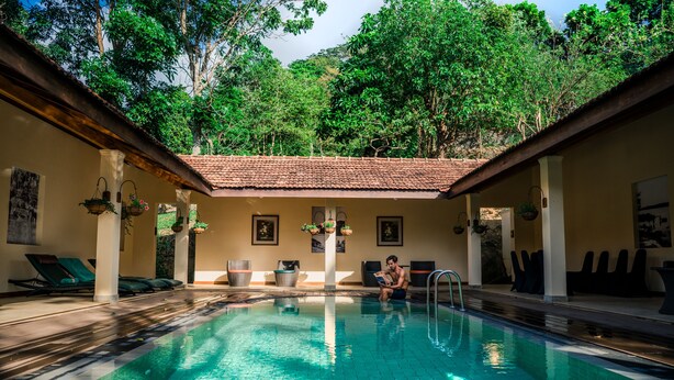 An indoor swimming pool with clear water, surrounded by lounge chairs and potted plants, set against a backdrop of lush greenery. - Hanthana Boutique Villa by Amaya (Kandy)