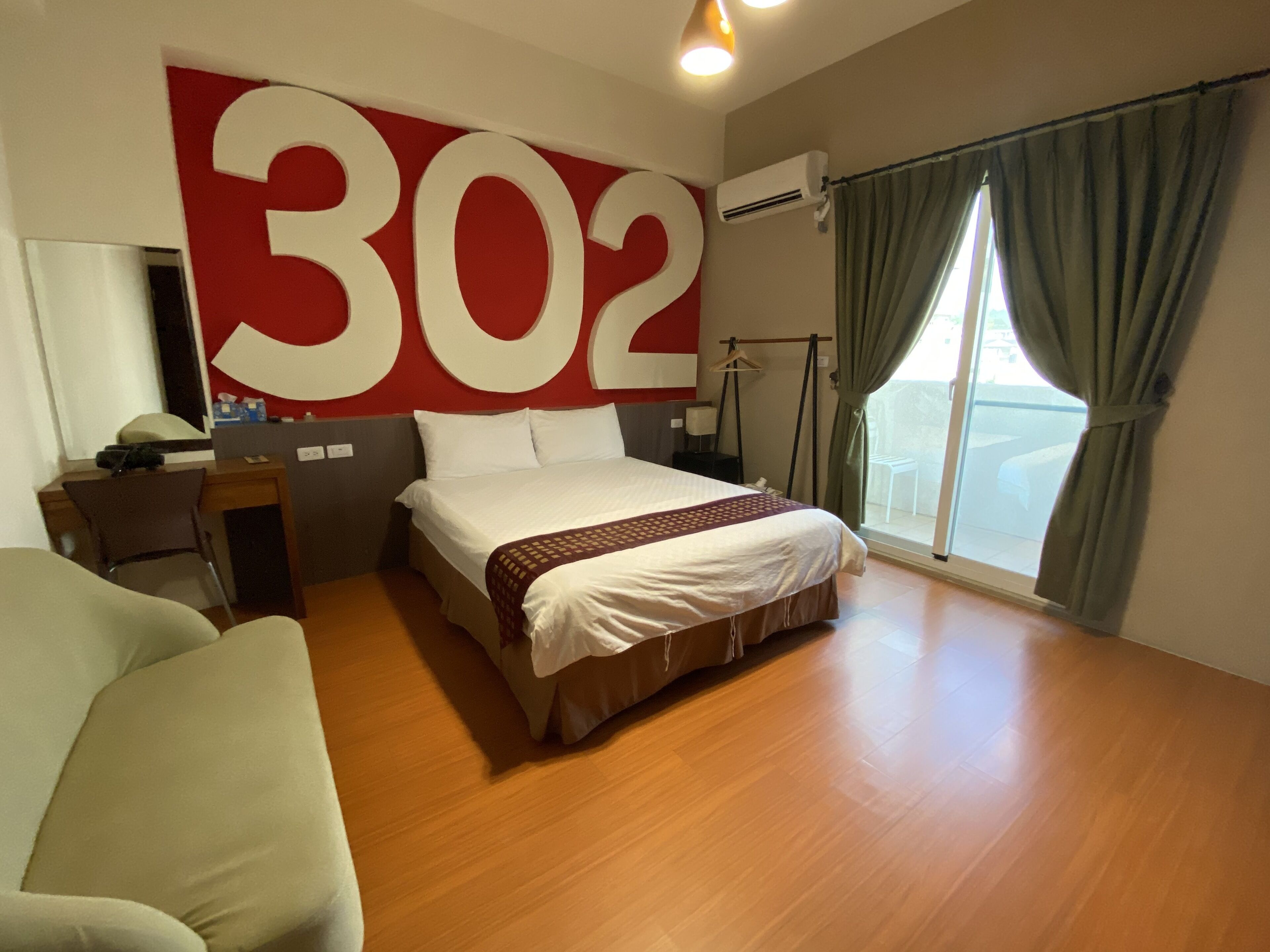 Une chambre d’hôtel avec un grand numéro « 302 » sur le mur, un lit, un bureau, une chaise et une vue par la fenêtre.