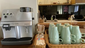 A coffee machine, a basket of coffee cups, and a kitchen area with utensils. - Happy Life Hostel (Taitung)