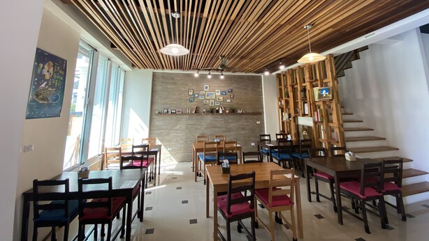 A modern dining area with wooden tables and chairs, a sloped ceiling with wooden beams, and a wall with framed pictures. - Happy Life Hostel (Taitung)