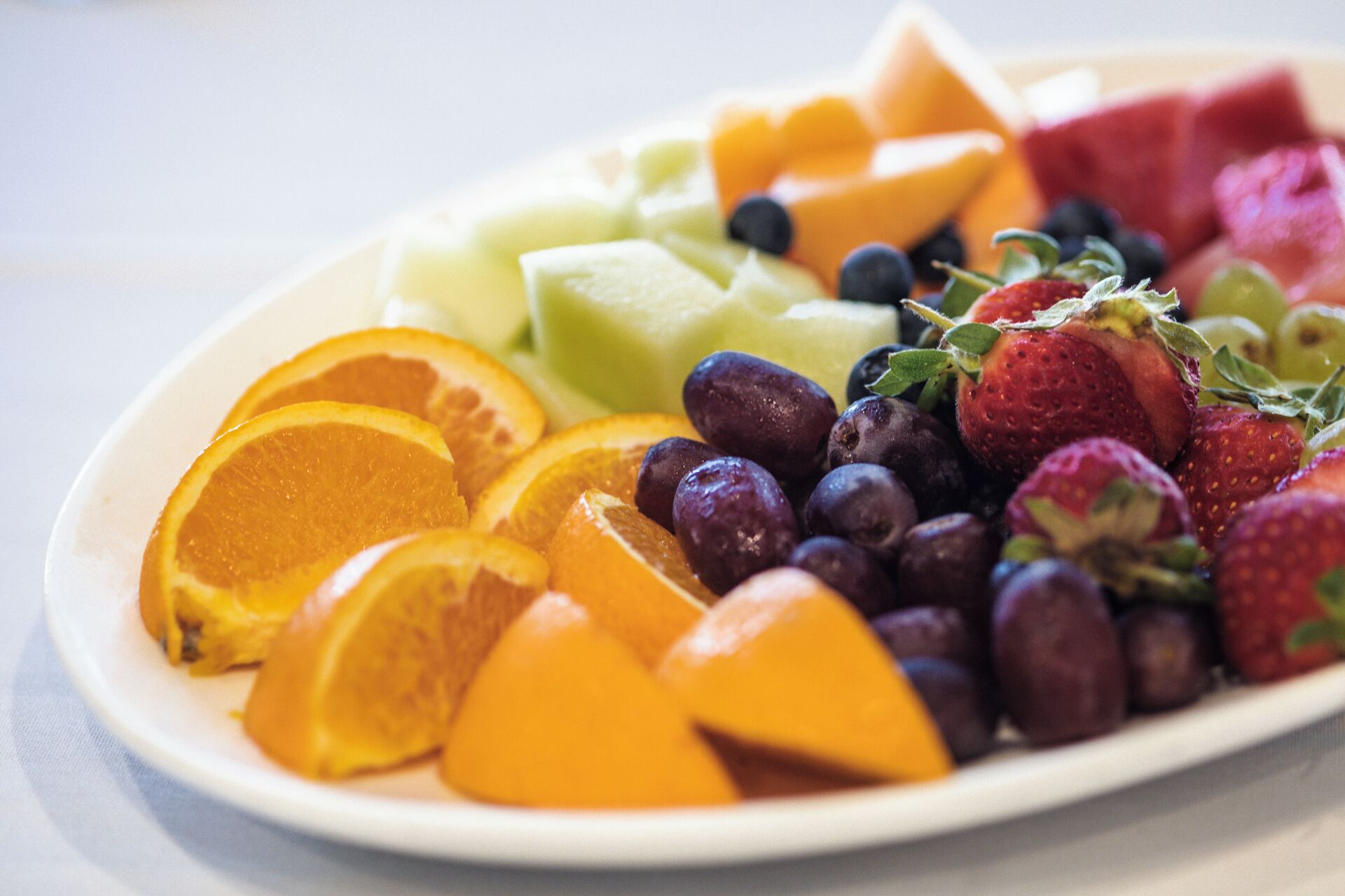 Une assiette de fruits variés, notamment des fraises, des myrtilles, des oranges et du melon.