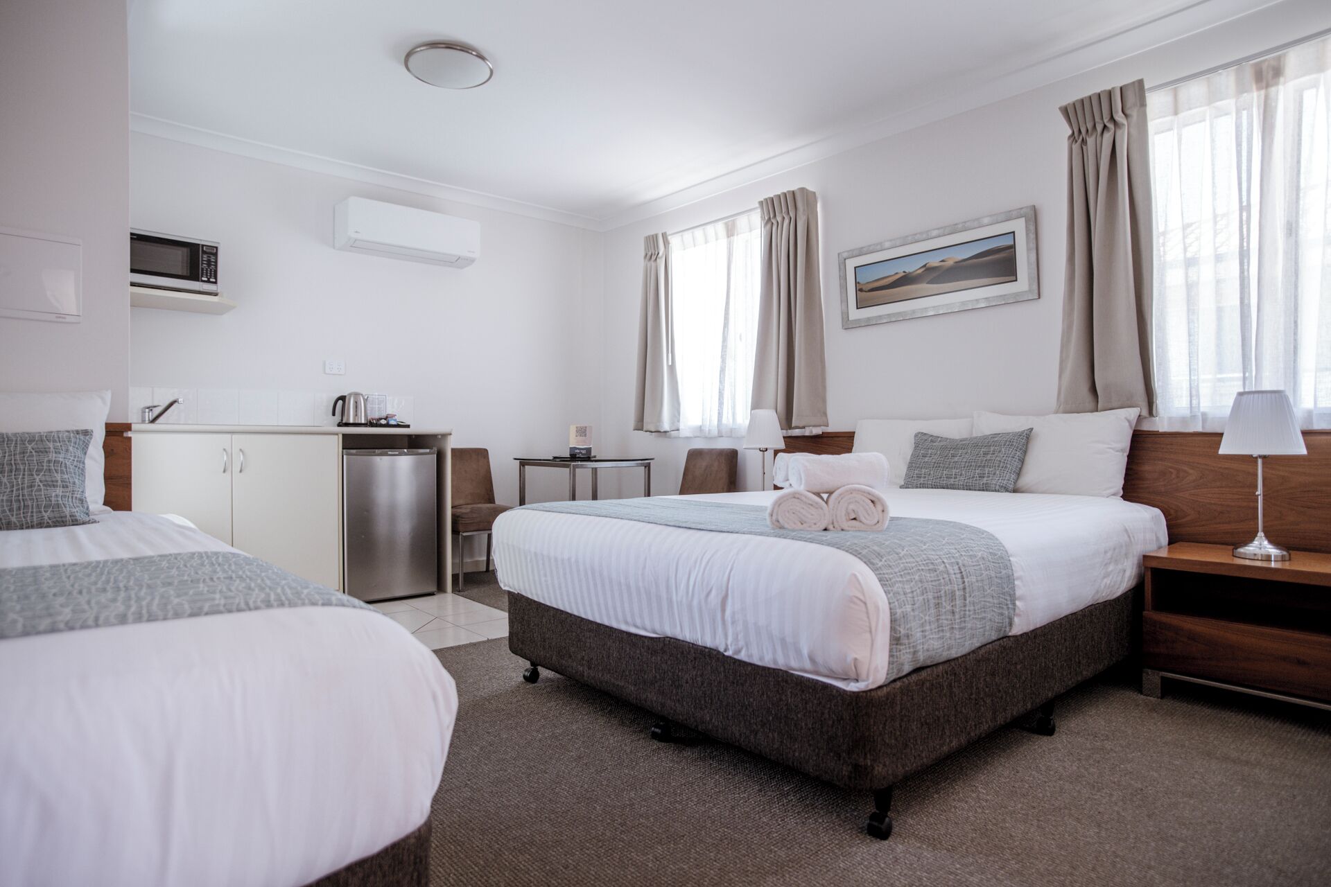 A hotel room with two beds, a kitchenette, a desk, and a view of a desert landscape.