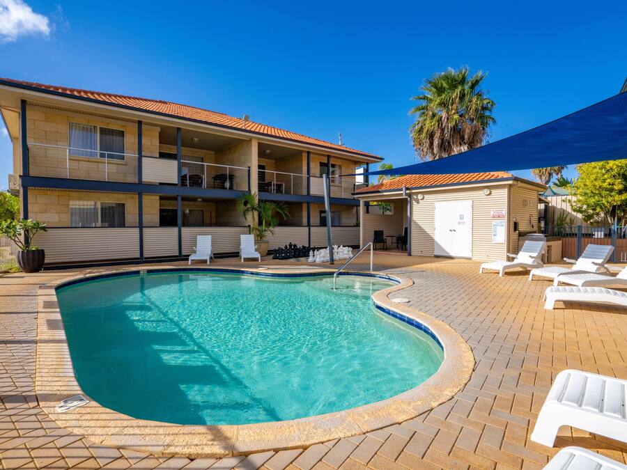 A swimming pool with a curved edge, surrounded by a brick patio. There are lounge chairs and a covered seating area.