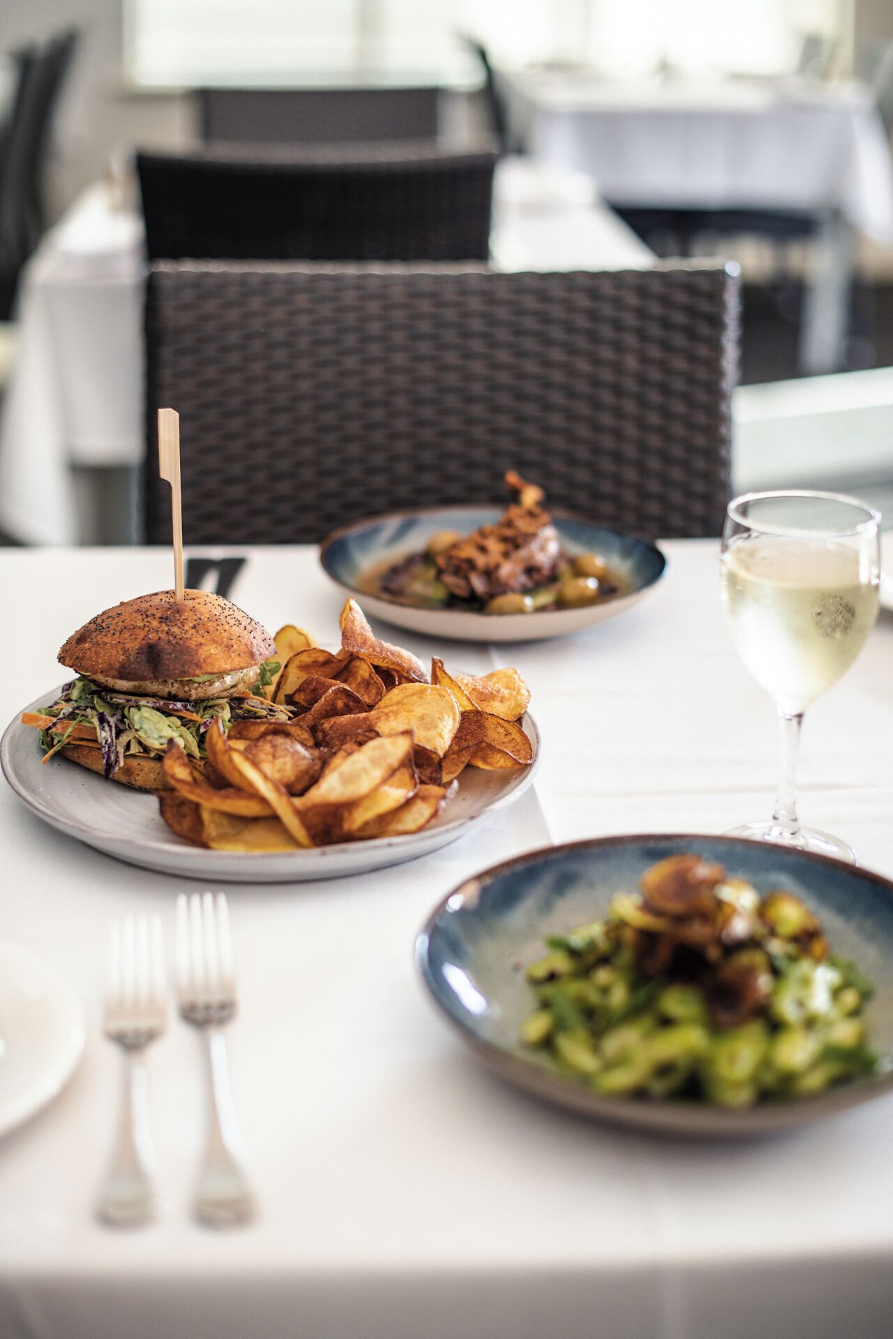 A dining table with plates of food, a glass of white wine, and cutlery.