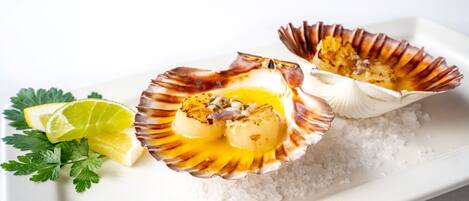 A plate with two scallops on a bed of salt, accompanied by a lime wedge and parsley.