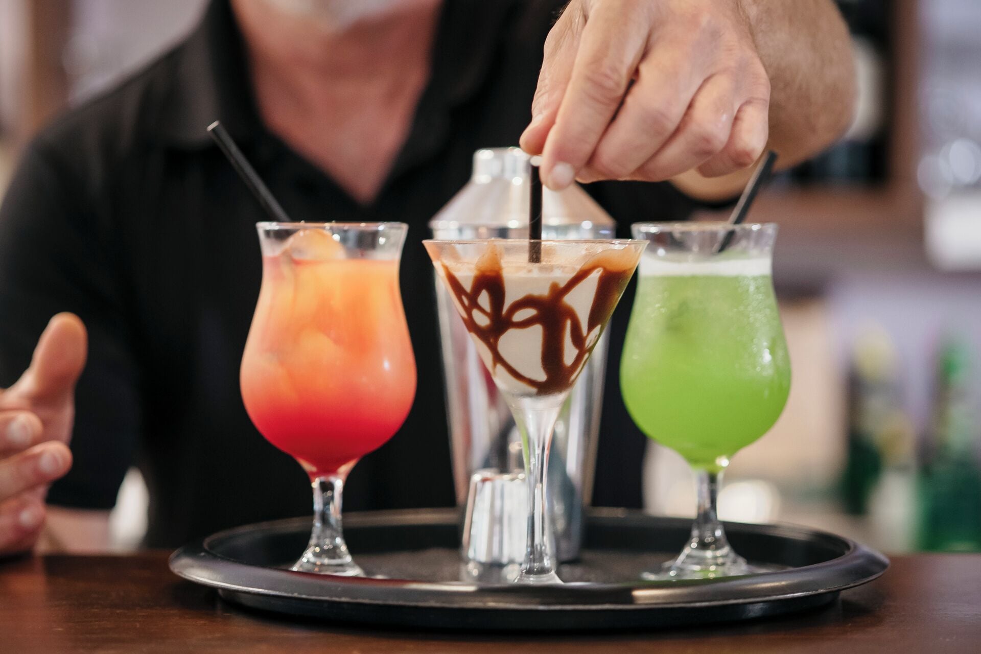 Three cocktails on a tray with a bartender's hand adding a garnish.