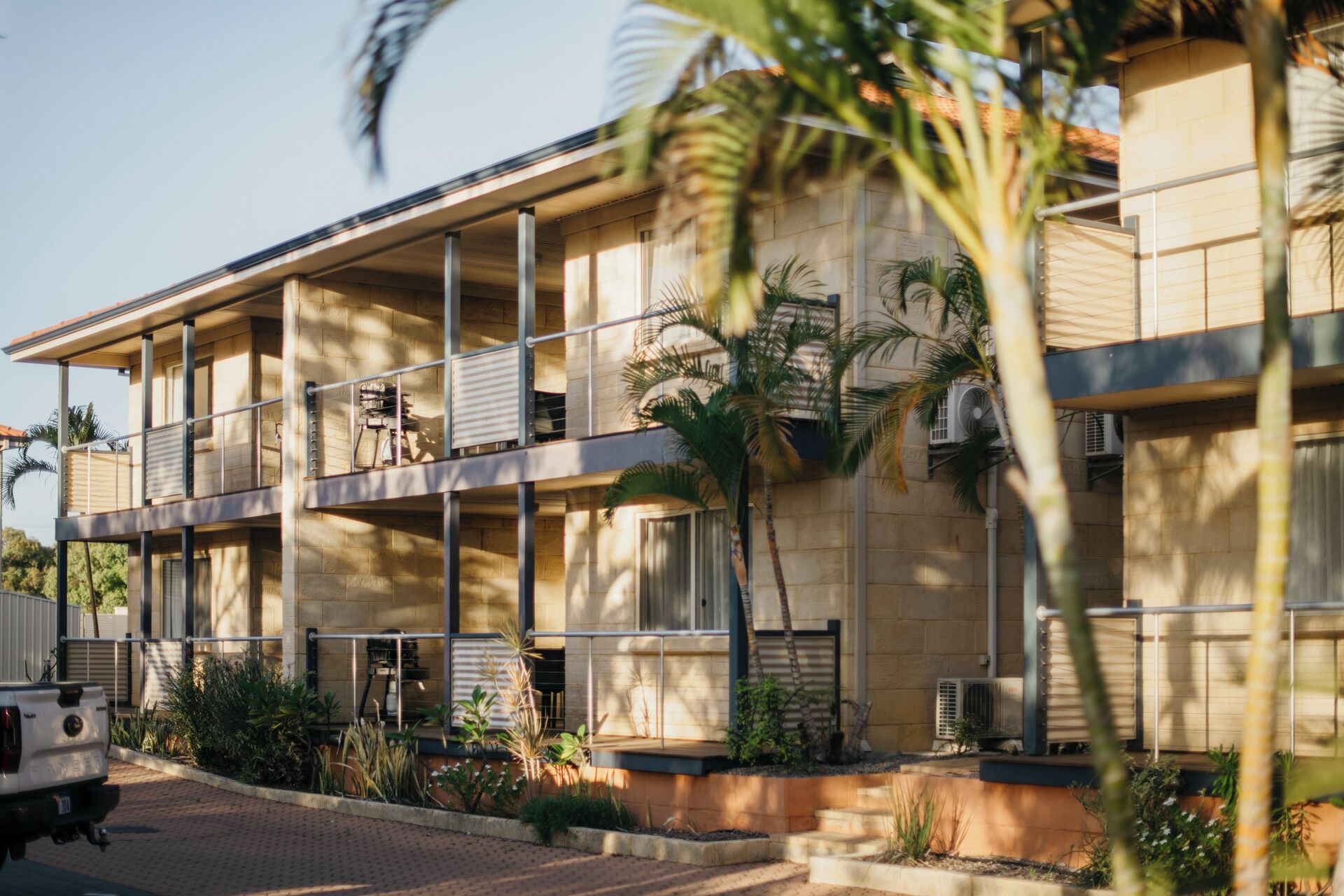 A multi-story hotel with balconies, air conditioning units, and a paved driveway.