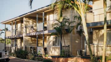 A multi-story hotel with balconies, air conditioning units, and a paved driveway.