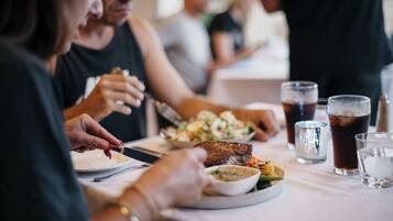 A dining table with plates of food, glasses of a dark beverage, and a person using a knife.