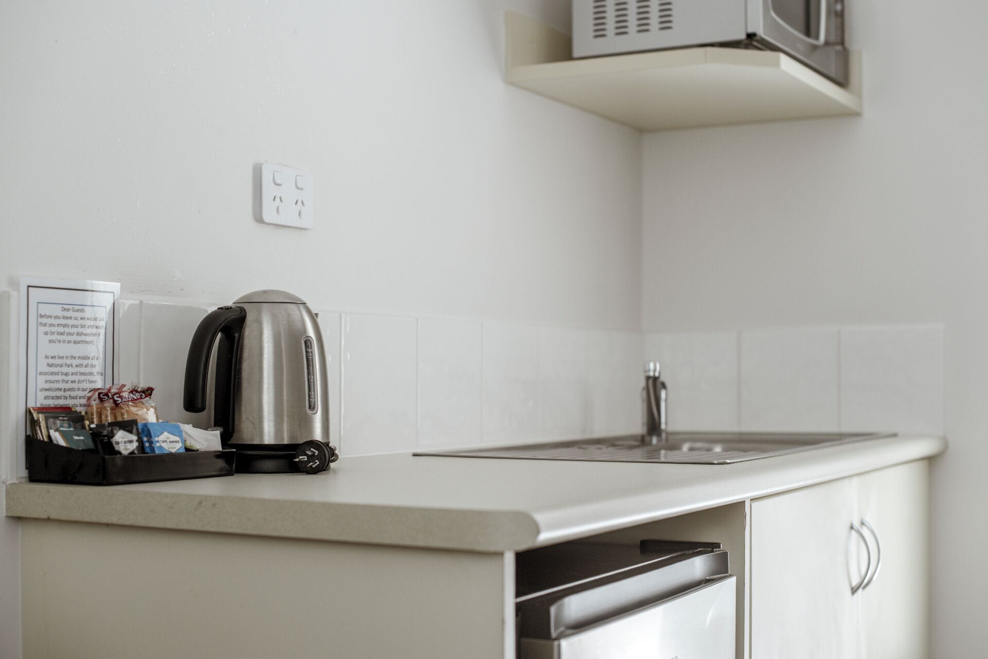 A kitchen with a kettle, a microwave, and a trash bin.