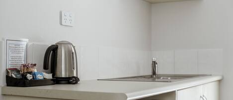 A kitchen with a kettle, a microwave, and a trash bin.