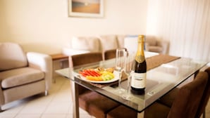 Een eetgedeelte met een glazen tafel, een fles champagne en een schaal met fruit.