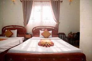 A hotel room with two single beds, a wooden headboard, a bedside table with a lamp, and a small table with a flower arrangement. - Golden Tulip Hotel (Nha Trang)