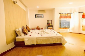 A neatly made bed with a white bedspread and pillows, a small table with a vase of flowers, and a framed picture on the wall. - Golden Tulip Hotel (Nha Trang)