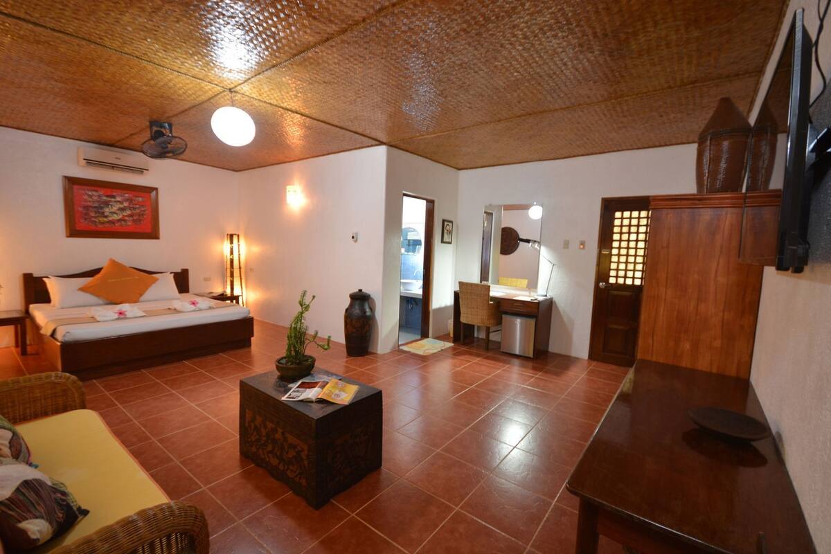 Una habitación con cama, escritorio, silla, mesita, planta y espejo.