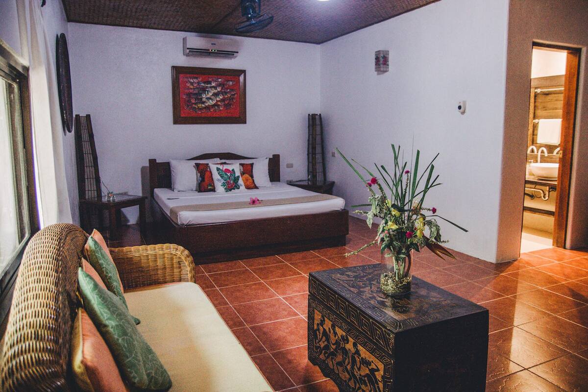 Un dormitorio con cama, sofá, un jarrón decorativo y cabecera de madera.