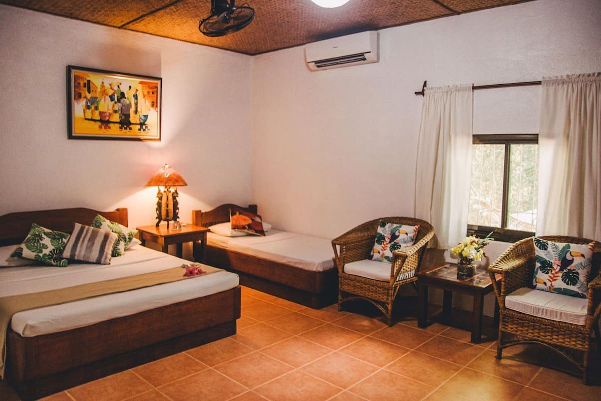 Una habitación con dos camas, una silla, una mesa, aire acondicionado y una ventana con cortinas.