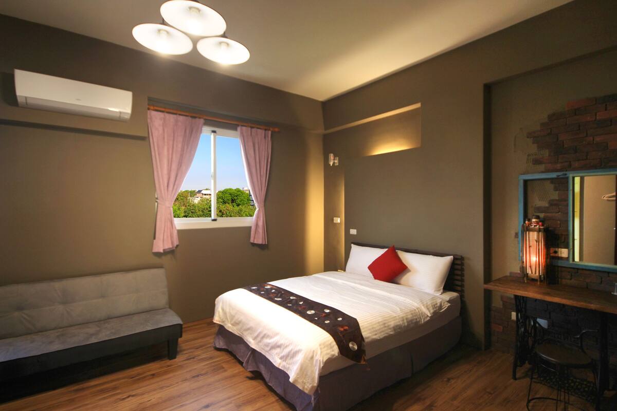Une chambre à coucher avec un lit, un banc, un bureau avec une chaise et une fenêtre avec des rideaux.