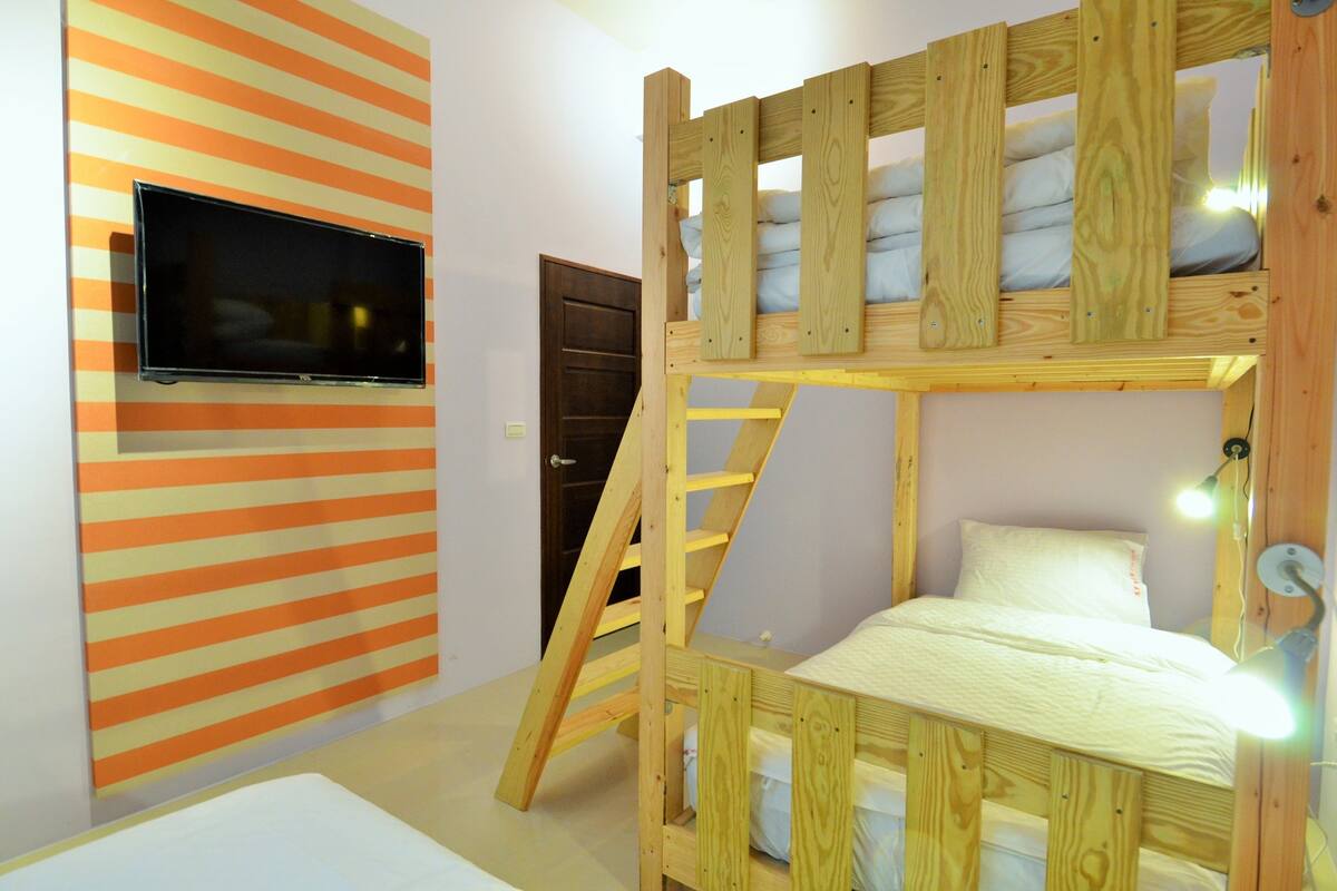 Un lit superposé avec un téléviseur fixé au mur, une échelle en bois et une porte.