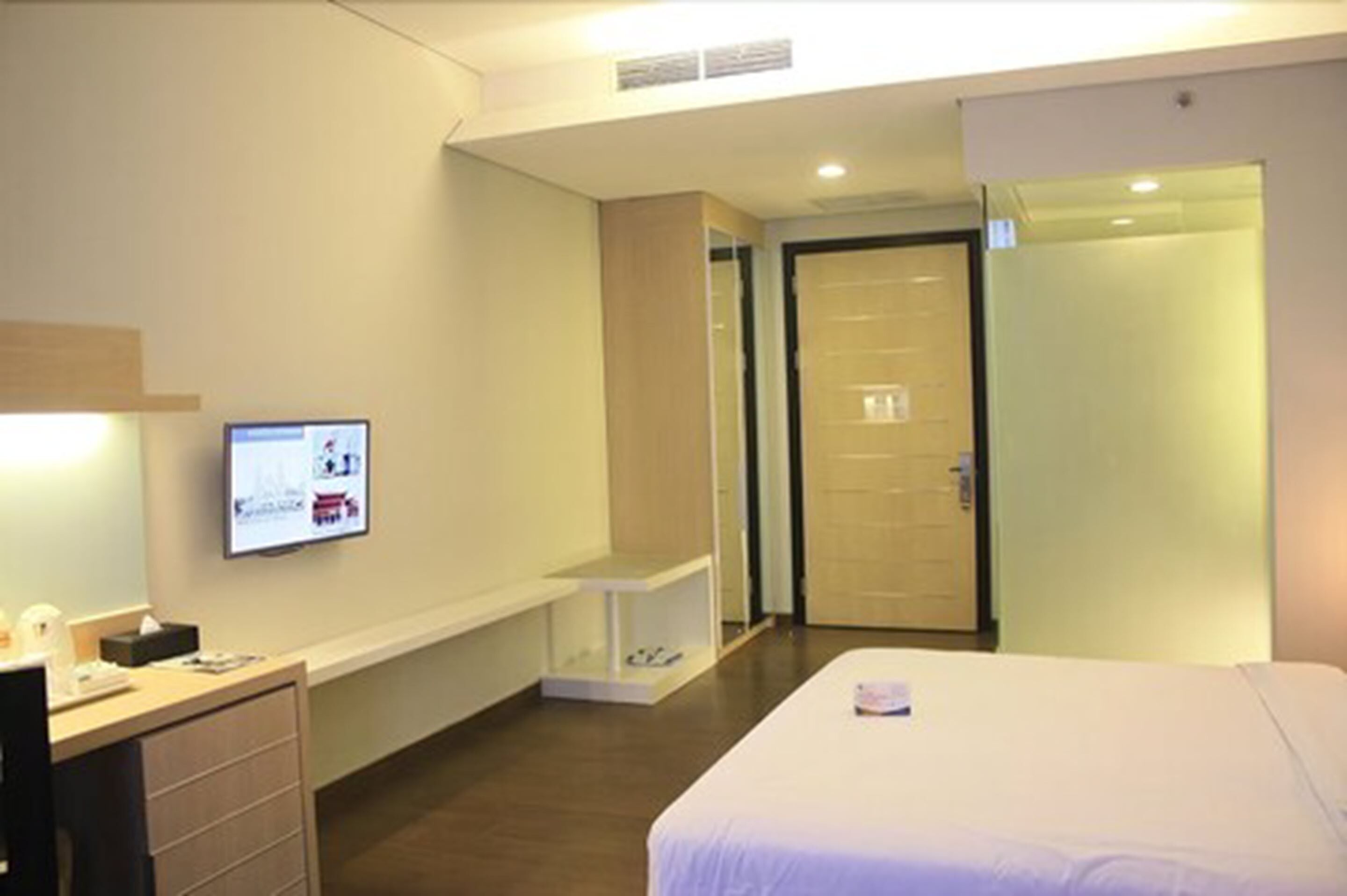 A hotel room with a bed, a desk with a computer, a small table, and a door.