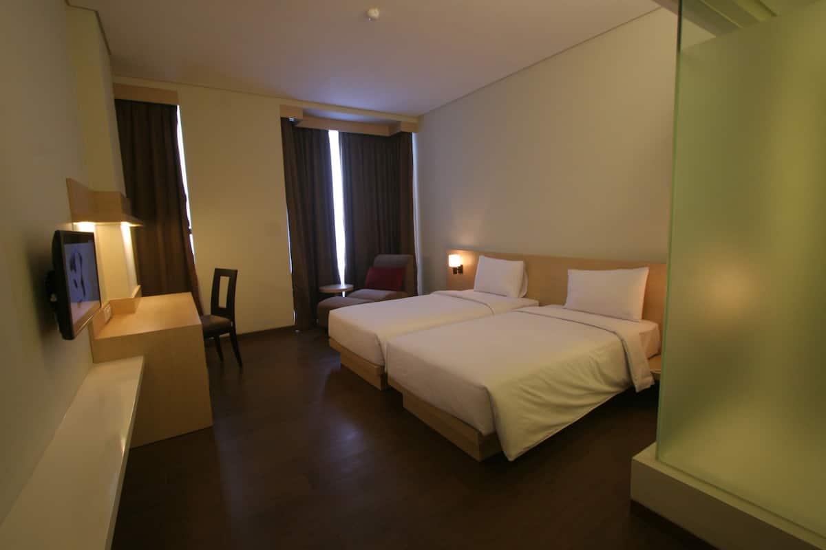 A hotel room with two beds, a desk, a chair, and a TV.