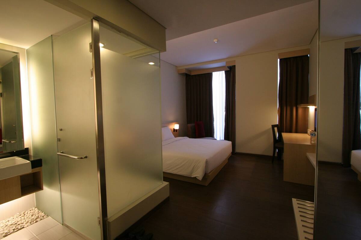 A hotel room with a bed, bedside table, and a mirror.