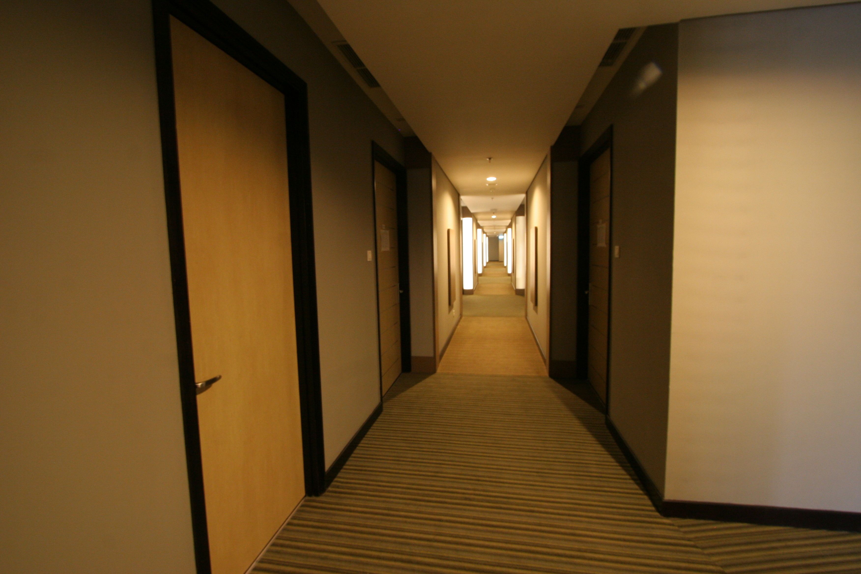 Pasillo de hotel con puertas a ambos lados, piso alfombrado y un largo corredor que lleva a un final luminoso.