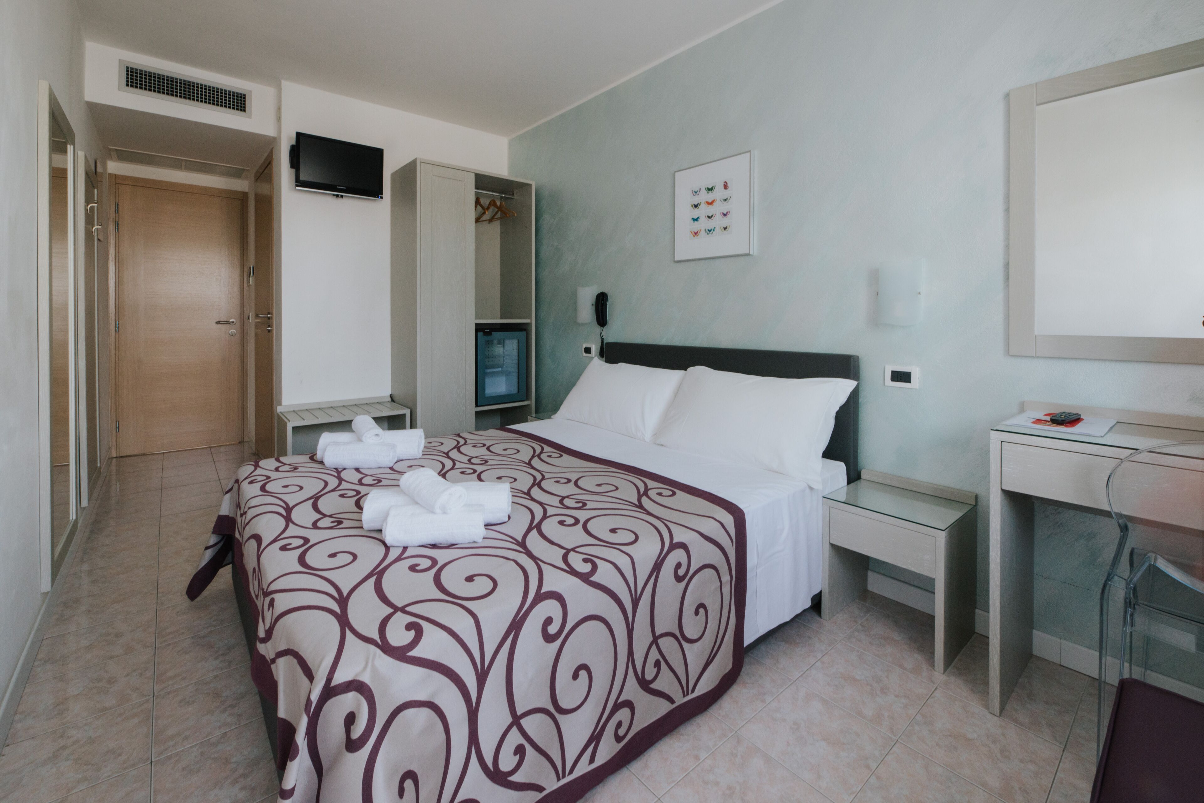 A hotel room with a bed, a desk, a chair, a wardrobe, and a television.