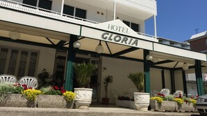 A hotel named "Hotel Gloria" with a covered entrance, outdoor seating area, and potted plants. - Hotel Gloria (Lignano Sabbiadoro)