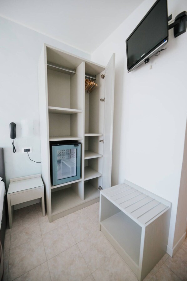 A room with a built-in wardrobe, a small bedside table, and a television mounted on the wall.