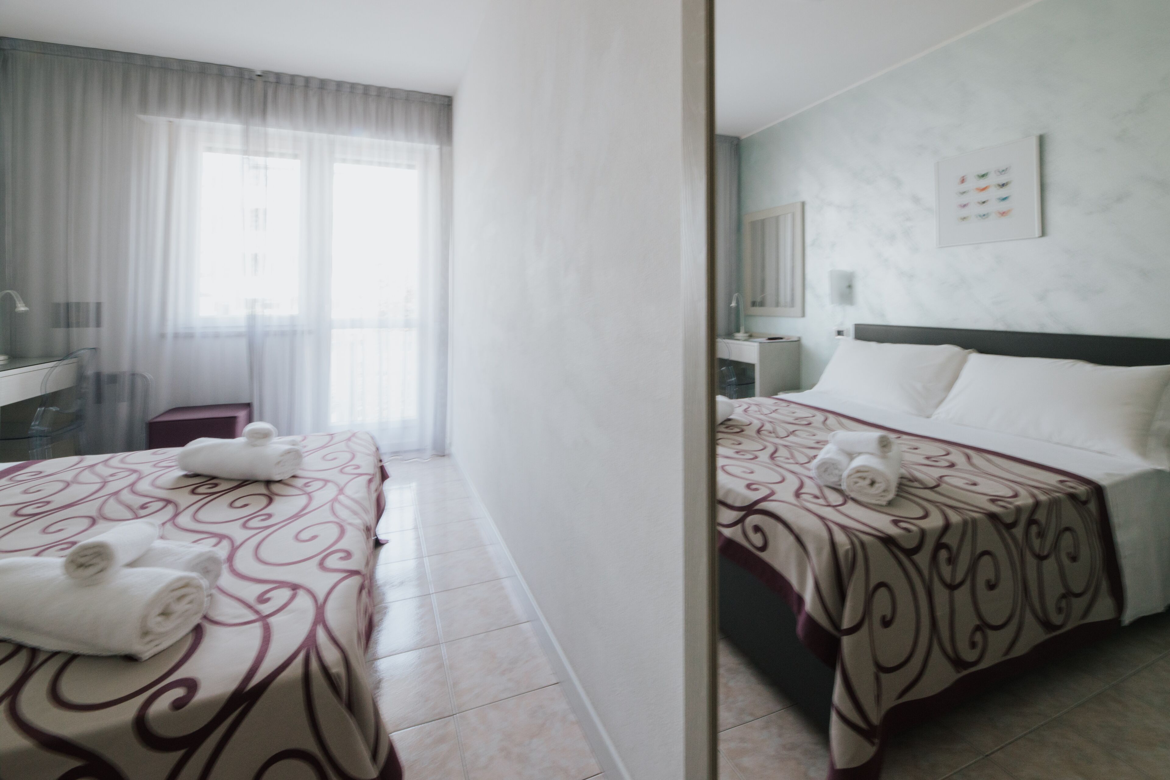 A hotel room with a large bed, a bedside table, a mirror, and a window with curtains.
