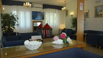A modern hotel lobby with dark blue sofas, a glass coffee table with decorative items, a red and white striped tent, and a large painting on the wall.
