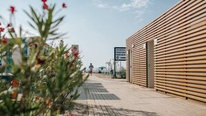 A wooden building with a sloped roof, a paved walkway, and a sign in the background. - Hotel Gloria (Lignano Sabbiadoro)