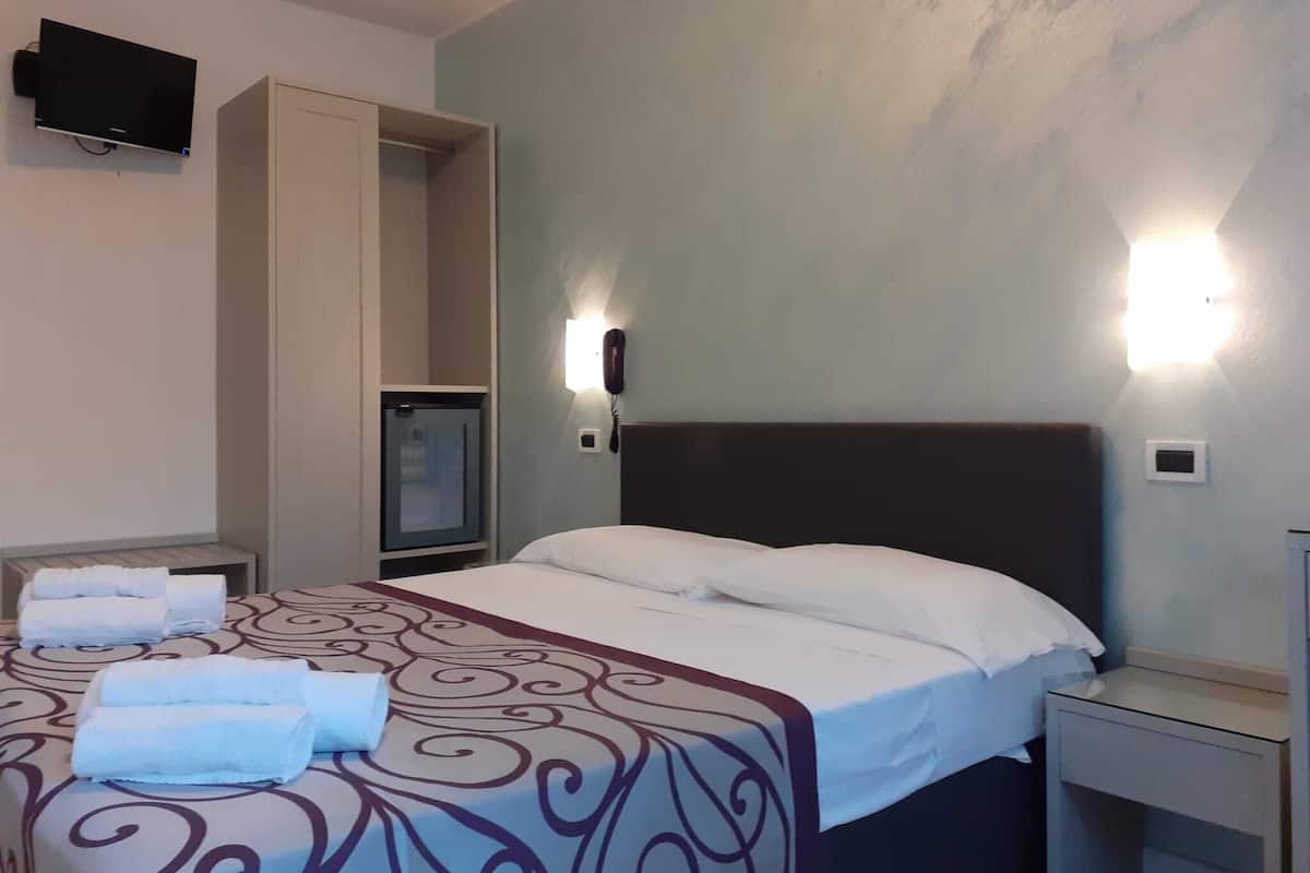 Una camera d'albergo con un letto, un comodino, una scrivania e un televisore a parete, oltre a un telefono.