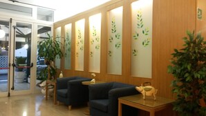 A reception area with two sofas, a small table, and a decorative pig statue. There is a large plant and a glass door leading outside. - Hotel Gloria (Lignano Sabbiadoro)