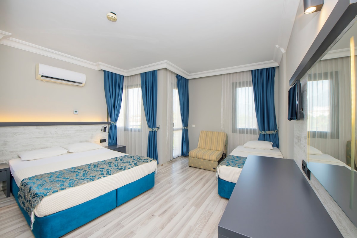 A modern hotel room with two beds, a sofa, a desk, and a large mirror.