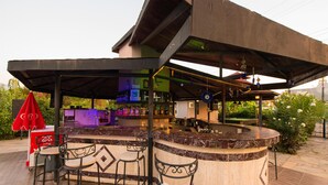 A bar area with a curved marble counter, metal chairs, and a red umbrella. - Golden Moon Hotel (Fethiye)