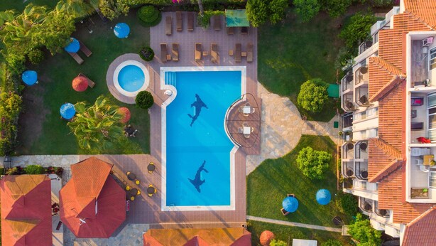 An aerial view of a hotel with a central swimming pool, outdoor seating areas, and lush landscaping. - Golden Moon Hotel (Fethiye)
