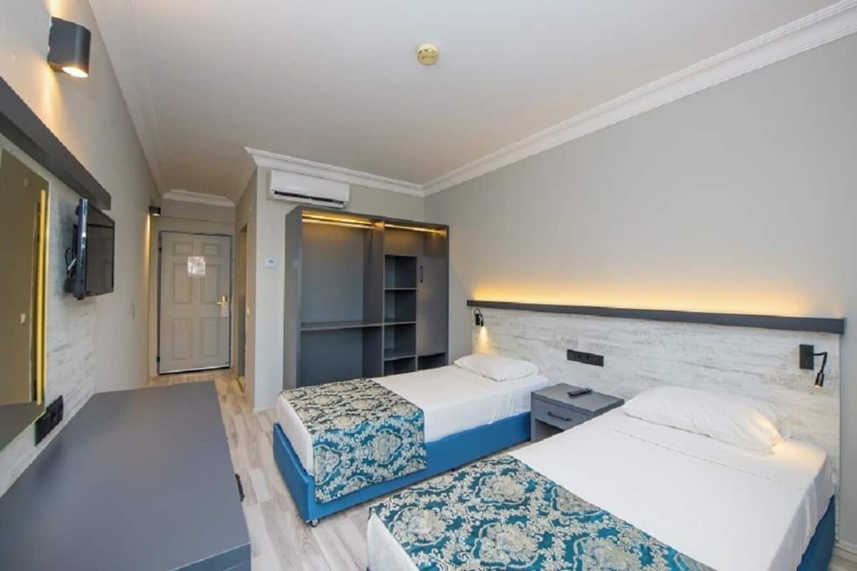 A hotel room with two beds, a desk, a wardrobe, and an air conditioning unit.